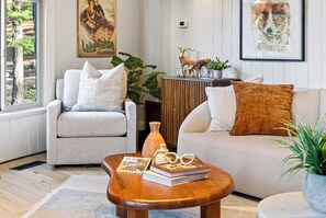 A living room with a sofa, armchair, and coffee table, featuring books and decorative items. - Redwood Home | Sauna + Hot Tub | Near Lifts + Village | Roundhouse at Northstar (Truckee)