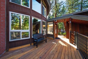 Una terraza de madera con un banco y un área cubierta, con vistas a un bosque.