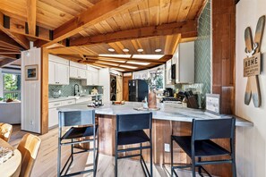 A modern kitchen with wooden beams, a central island with bar stools, and a herringbone-patterned backsplash. - Redwood Home | Sauna + Hot Tub | Near Lifts + Village | Roundhouse at Northstar (Truckee)