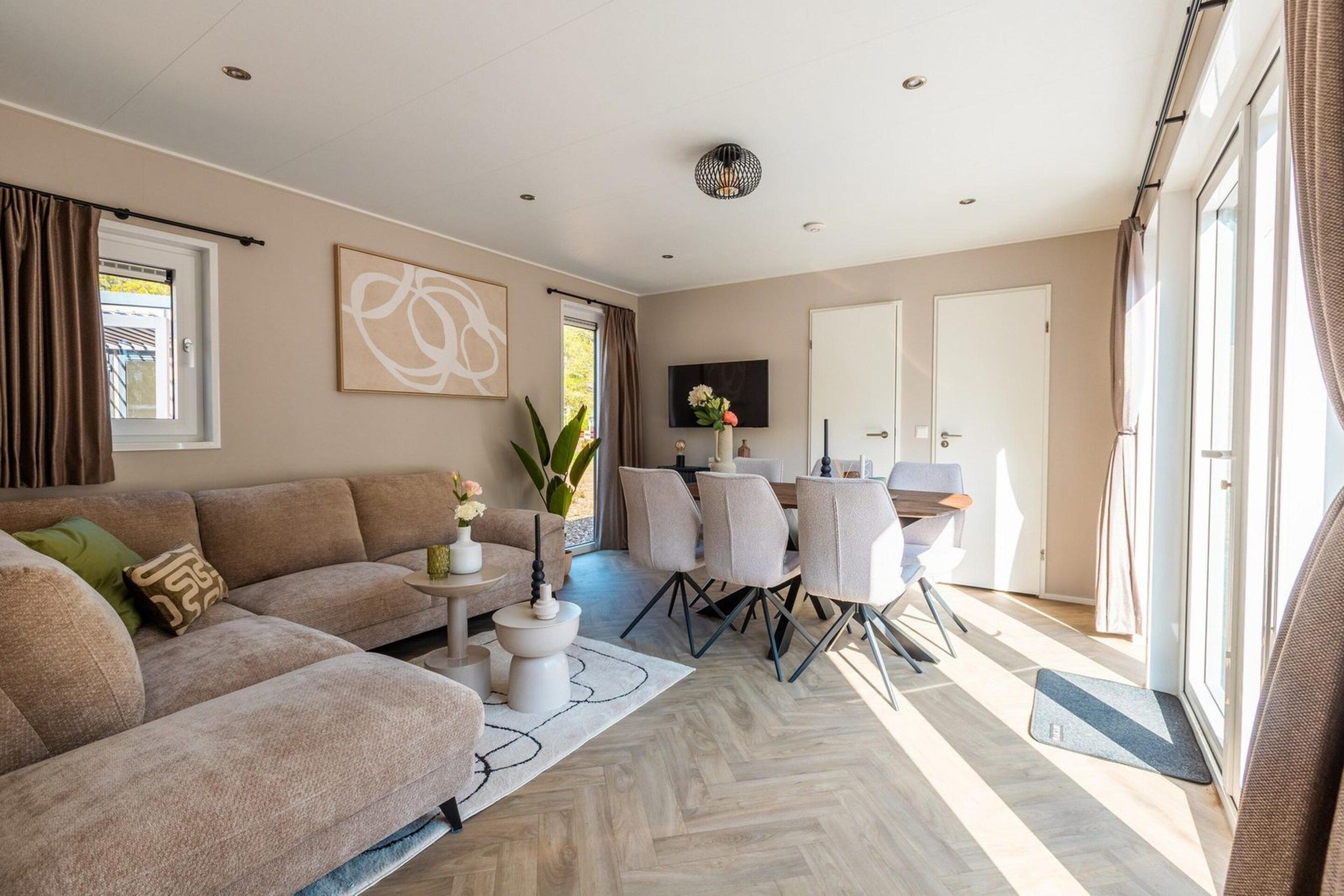 Ein modernes Wohnzimmer mit einer Couch, einem Esstisch mit Stühlen und einem an der Wand befestigten Fernseher.
