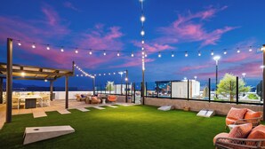 An outdoor patio with artificial grass, seating, and string lights against a twilight sky. - 2 Condos + Rooftop Pool + Gym + Sauna | Desert Ridge | Azur by AvantStay (Phoenix)