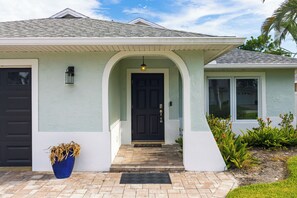 Une maison avec une porte d’entrée de couleur sombre, une façade de couleur claire et un petit porche.