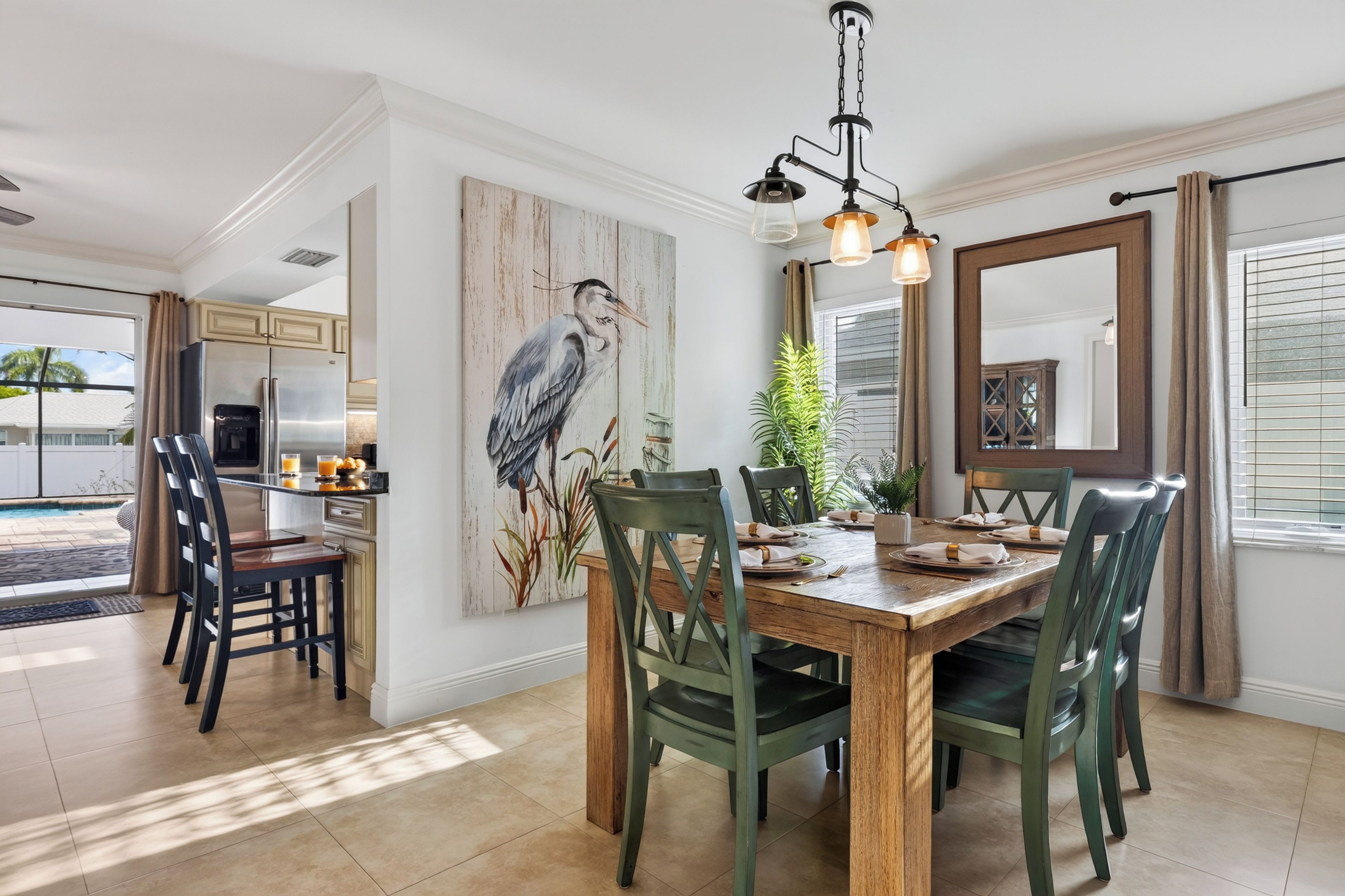 Un coin repas avec une table en bois, des chaises vertes et un grand tableau représentant un oiseau accroché au mur.