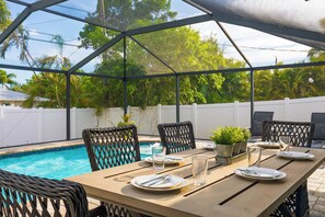 Une terrasse extérieure avec une piscine, une table à manger, des chaises et un espace abrité.