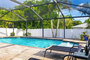 Ein Poolbereich mit überdachter Terrasse, einem Tisch mit Stühlen und einer Champagnerflasche.