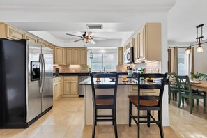 A modern kitchen with a central island, stainless steel appliances, and a ceiling fan. - Naples Park Stay • Private Pool + Lanai • Near Vanderbilt Beach | Lanai & Light (Naples)