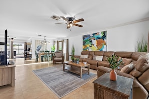 Ein großzügiges Wohnzimmer mit einer braunen Ledersofa, einem Holztisch und einem Essbereich mit grünen Stühlen.