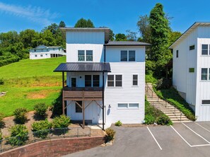 A two-story building with a covered porch and a parking area in front. - Blue Ridge Views + Balcony + Two Living Rooms | Downtown | Tranquil River Home (Asheville)
