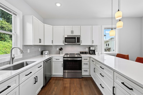 Une cuisine moderne avec des meubles blancs, des appareils en acier inoxydable et un plancher en bois.