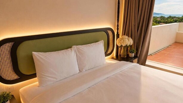 A hotel room with a bed, a nightstand, a vase with flowers, and a view of the outdoors. - Asteria Ocean Residence (Da Nang)