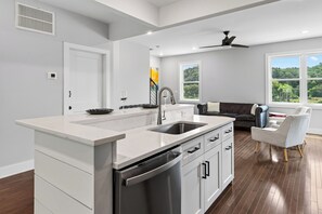 A modern kitchen with a built-in dishwasher and a large window overlooking a forest. - Balcony + River Views + Full kitchen | River Arts District | Sage House (Asheville)