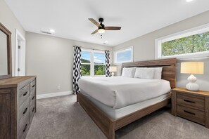 Un dormitorio con cama, mesitas de noche, cómoda, ventilador de techo y ventana con persianas.