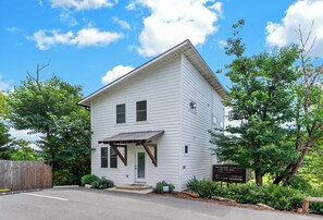 A two-story white house with a porch, surrounded by greenery and a wooden fence. - Balcony + River Views + Full kitchen | River Arts District | Sage House (Asheville)