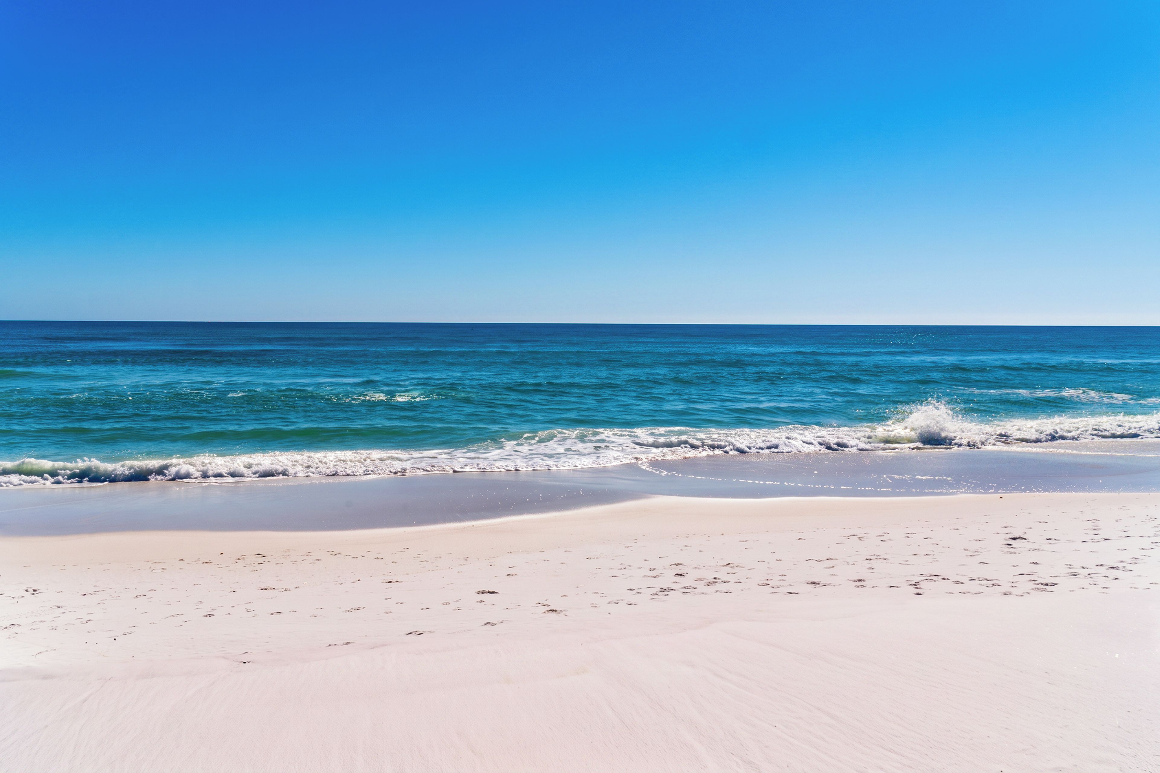 Une plage avec une eau d’un bleu limpide et un rivage sablonneux.