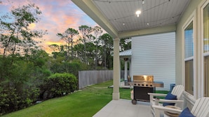 A covered patio with a grill, outdoor seating, and a view of the backyard. - 6-Seat Golf Cart + Arcade + Bunk Room | Beach Walk + Pool | Maré 33 (Miramar Beach)