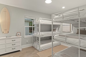 A bunk bed room with a surfboard, a window, and a dresser. - 6-Seat Golf Cart + Arcade + Bunk Room | Beach Walk + Pool | Maré 33 (Miramar Beach)