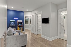Una sala de estar moderna con un sofá gris, una consola de videojuegos y un televisor de pantalla plana montado en la pared.