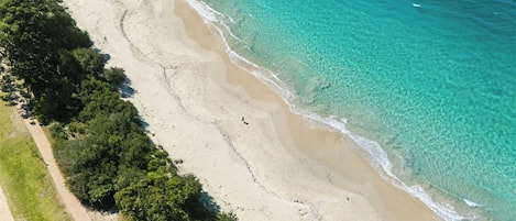 Oversigtsbillede af en strand med klart turkis vand, en sandstrand og en sti ned til stranden.