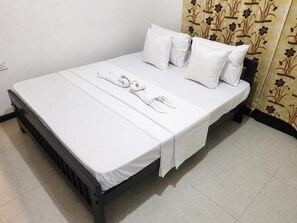 Ein Einzelbett mit weißer Bettwäsche und Kissen, ein schwarzer Kopfteil und ein Vorhang mit Blumenmuster.