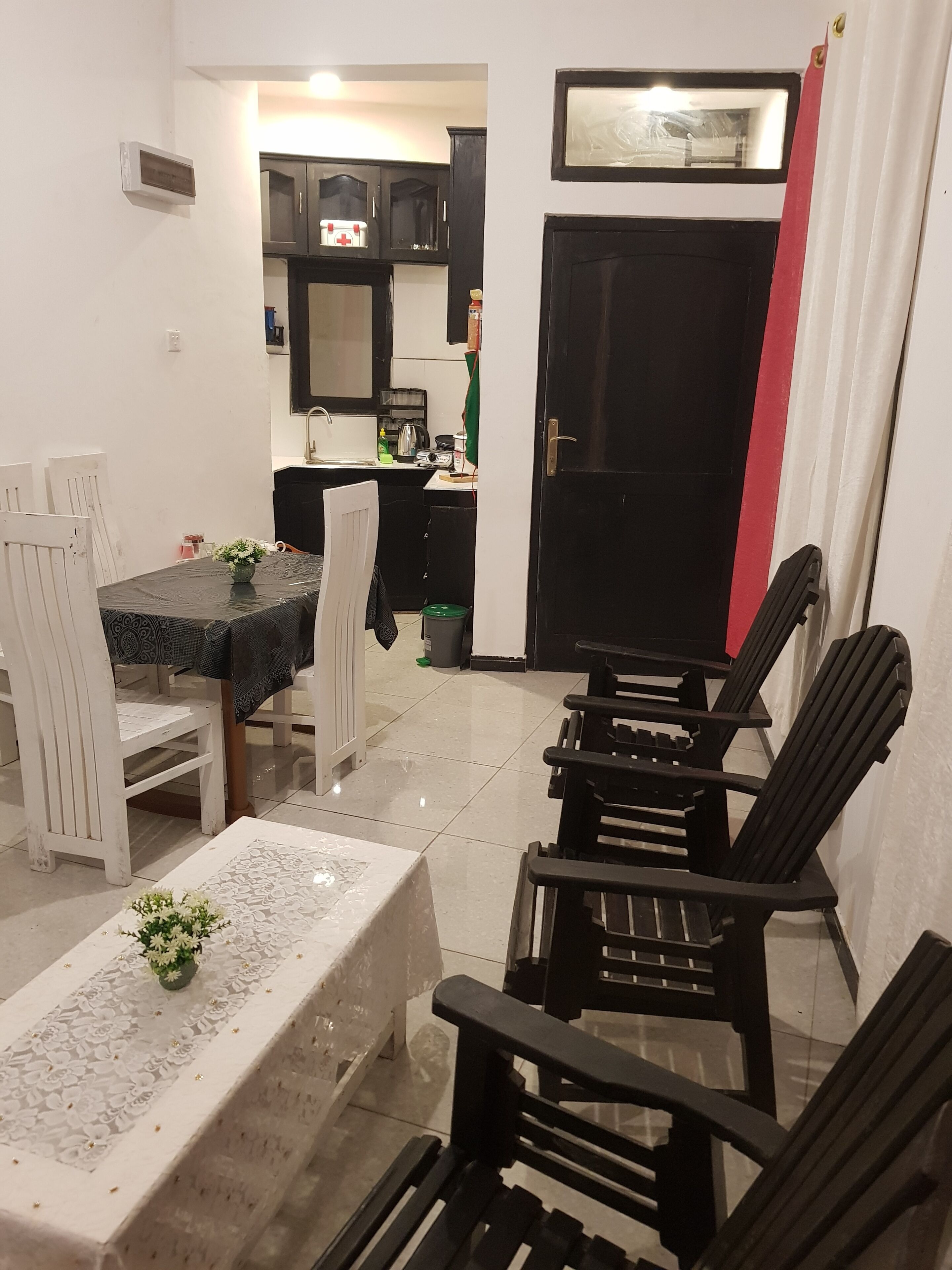 A dining area with a table set for four, a kitchen in the background, and a black door with a red stripe.