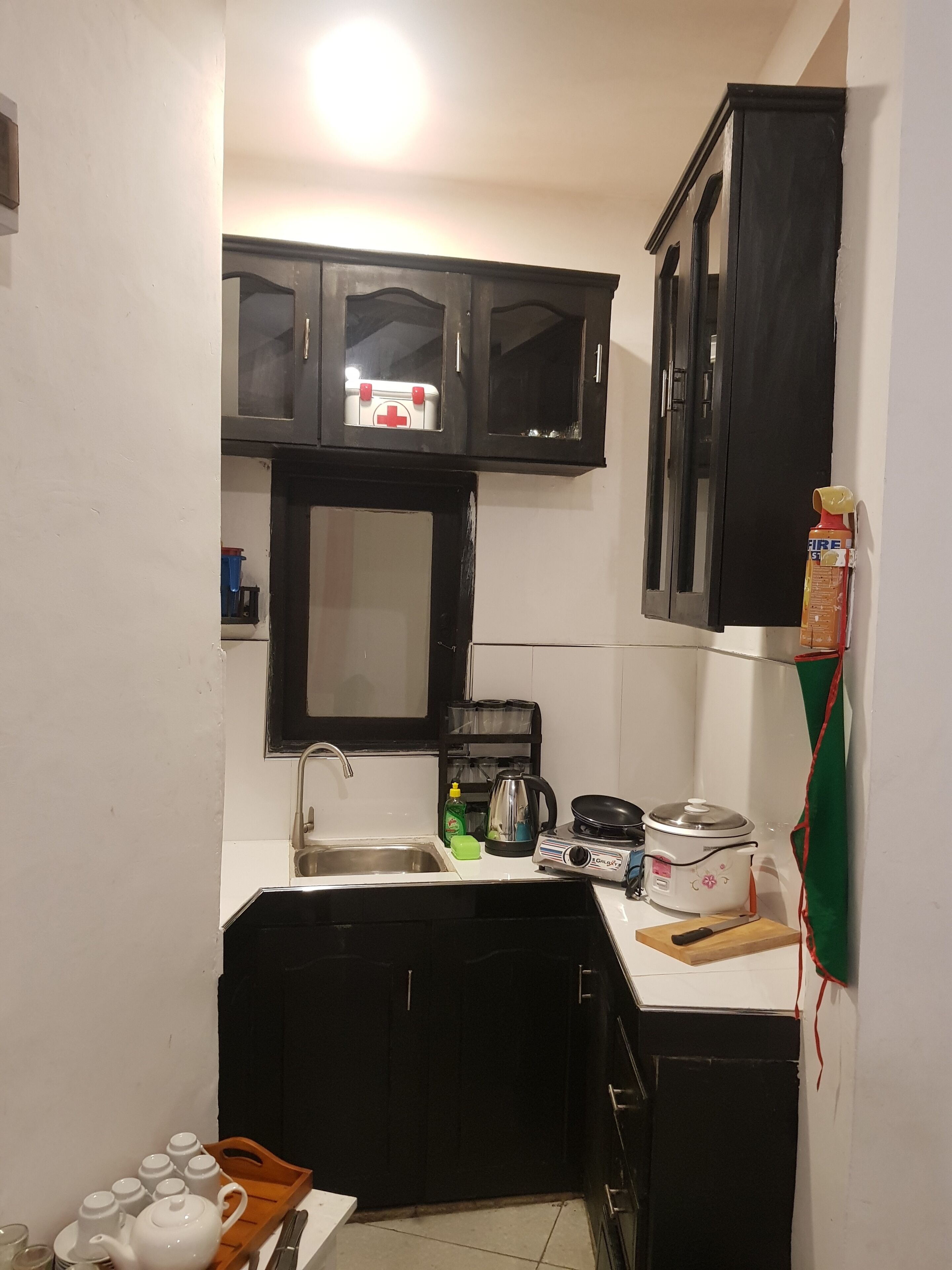 A compact kitchen with a sink, a stove, and a microwave. There is a cabinet above the sink and a shelf with kitchen items.