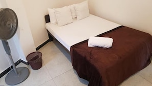 A single bed with a brown bedspread and white pillows, a standing fan, and a small trash bin. - Shalom View Homestay  (Kandy)