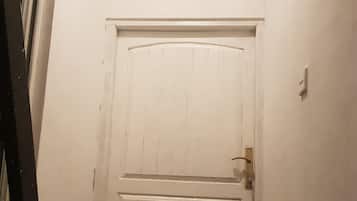 A white door with a small window above it, a metal ladder to the left, and a doormat on the floor.