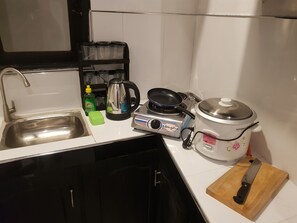 Una cocina con un lavamanos, una estufa a gas, un hervidor, una olla de cocción lenta y una tabla de cortar con un cuchillo.
