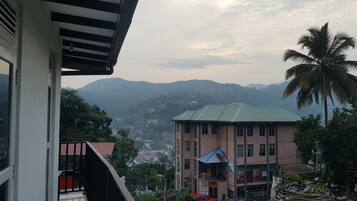 A multi-story building with a flat roof, a balcony, and a view of a hilly landscape in the background.