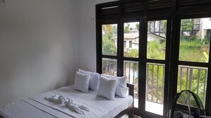A bedroom with a bed, pillows, and a window with a view of greenery and buildings. - Shalom View Homestay  (Kandy)