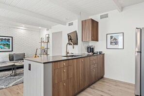 A modern kitchen with a central island, wooden cabinets, and stainless steel appliances. - The Weekend | 2 Suites • Boutique Stay in Palm Springs, Private Patio, Pool (Palm Springs)