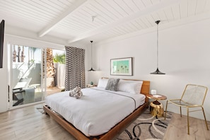 A modern bedroom with a large bed, a chair, a small table, and a view of the outdoors. - The Weekend | 2 Suites • Boutique Stay in Palm Springs, Private Patio, Pool (Palm Springs)