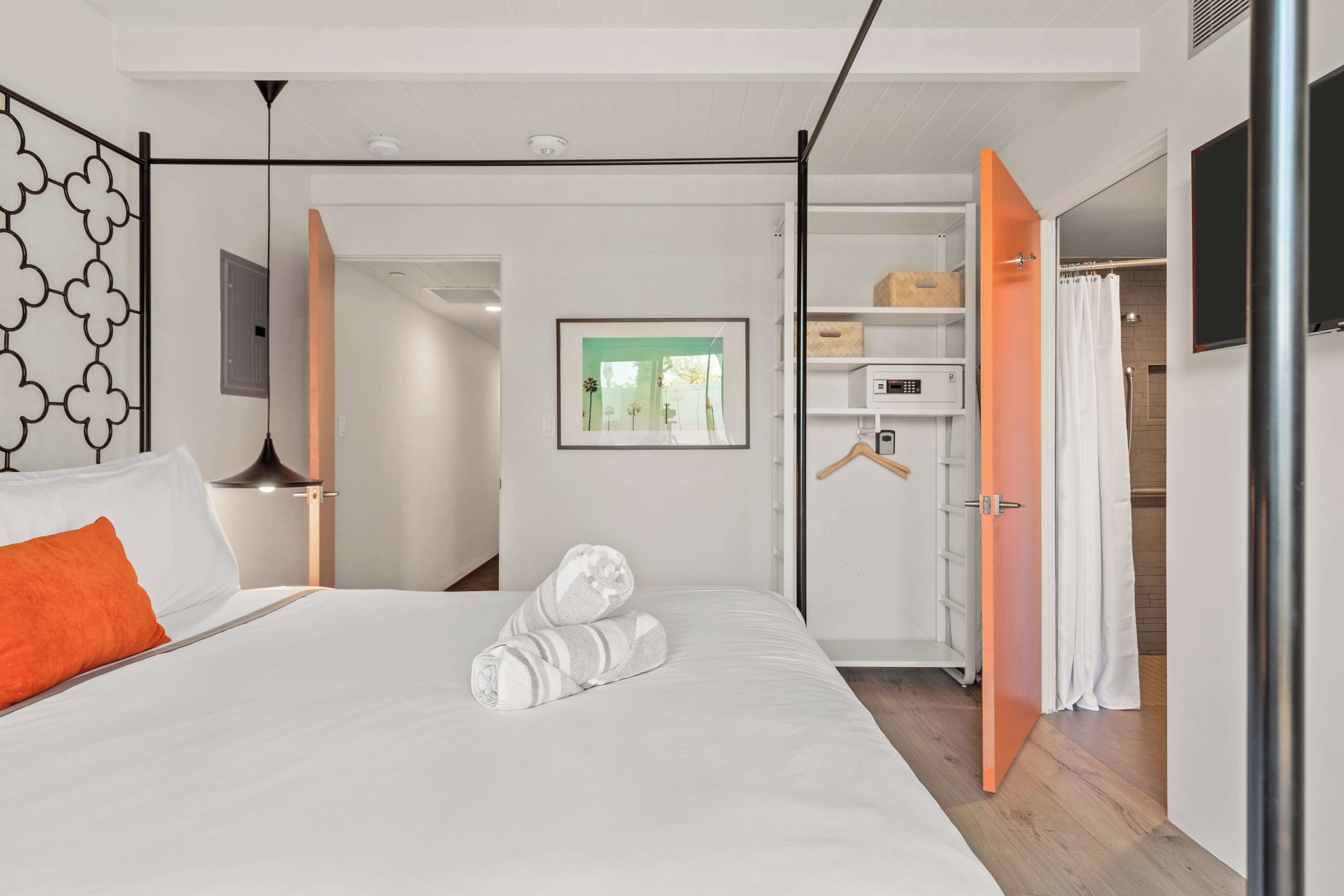 A modern hotel room with a bed, a wardrobe, a mirror, and a picture on the wall.