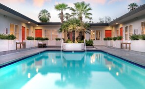 A swimming pool with a white planter in the center, surrounded by palm trees and a building with red doors. - The Weekend | 2 Suites • Boutique Stay in Palm Springs, Private Patio, Pool (Palm Springs)