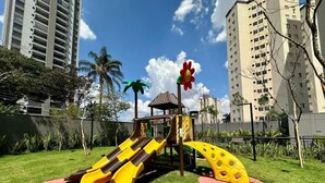 A playground with slides and climbing structures, surrounded by grass and trees, with buildings in the background. - 10% Off  Pôr do sol  GRU Airport 4km  2 Dorms (Guarulhos)
