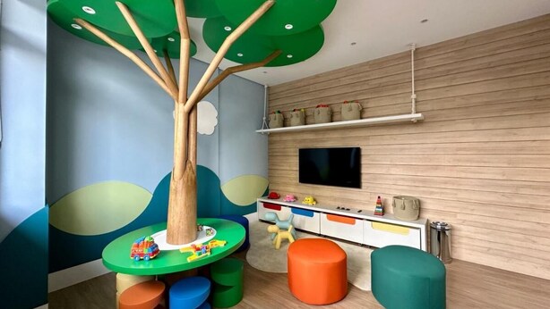 A children's play area with a tree-shaped table, colorful stools, and a television on the wall. - 10% Off  Pôr do sol  GRU Airport 4km  2 Dorms (Guarulhos)