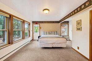A bedroom with a large bed, two windows, an exit sign, and a decorative wall border. - Alpine Chalet + Decks + Game Room | Near Ski + Lake | Stillwood (Stateline)