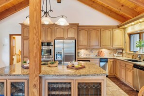 Una cocina con armarios de madera, un refrigerador de acero inoxidable, horno empotrado y encimera de granito.