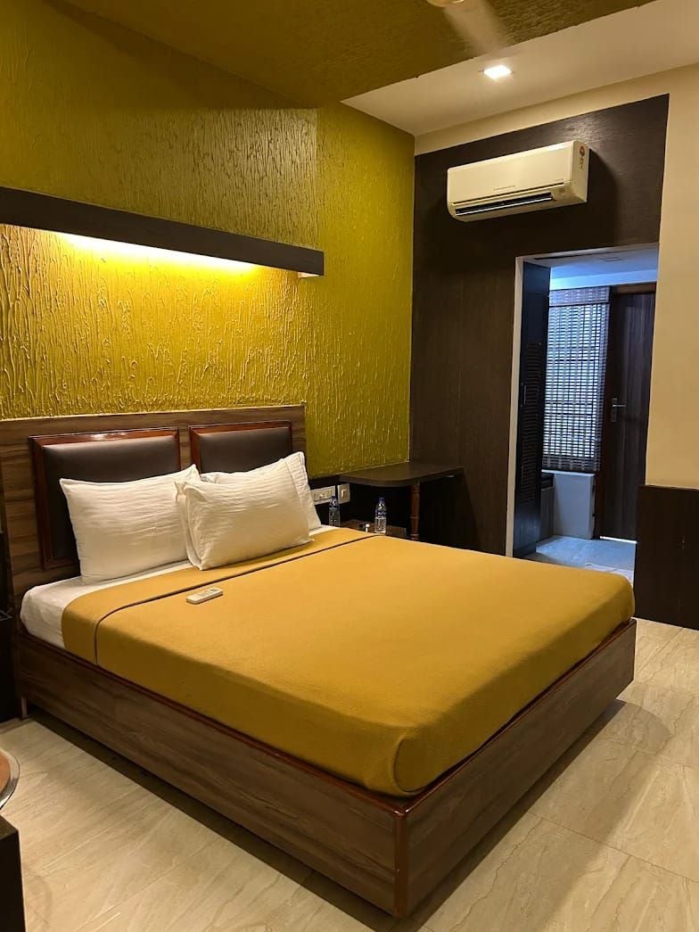 A hotel room with a bed, bedside table, and an air conditioning unit.