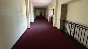 Un largo pasillo con alfombra roja, paredes blancas y una pared de piedra decorativa a la derecha.