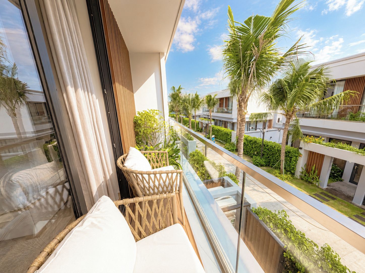 A balcony with wicker furniture and a view of a residential area with palm trees and modern buildings.
