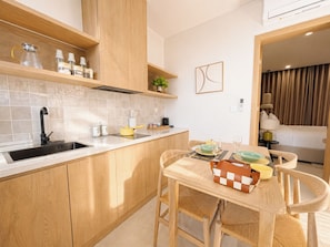 A modern kitchen with wooden cabinets, a built-in sink, and a dining area with a table set for two. - Sonasea Villas Collection Lagom  (Phu Quoc)
