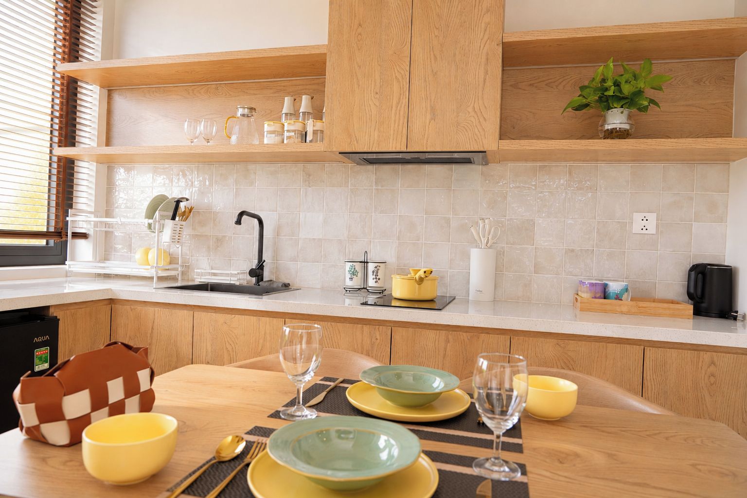 A modern kitchen with wooden cabinets, a tiled backsplash, and a dining area set with yellow and green plates, bowls, and glasses.