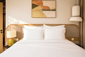 A neatly made bed with white linens, a bedside lamp, and a wall-mounted abstract painting. - Sonasea Villas Collection Lagom  (Phu Quoc)