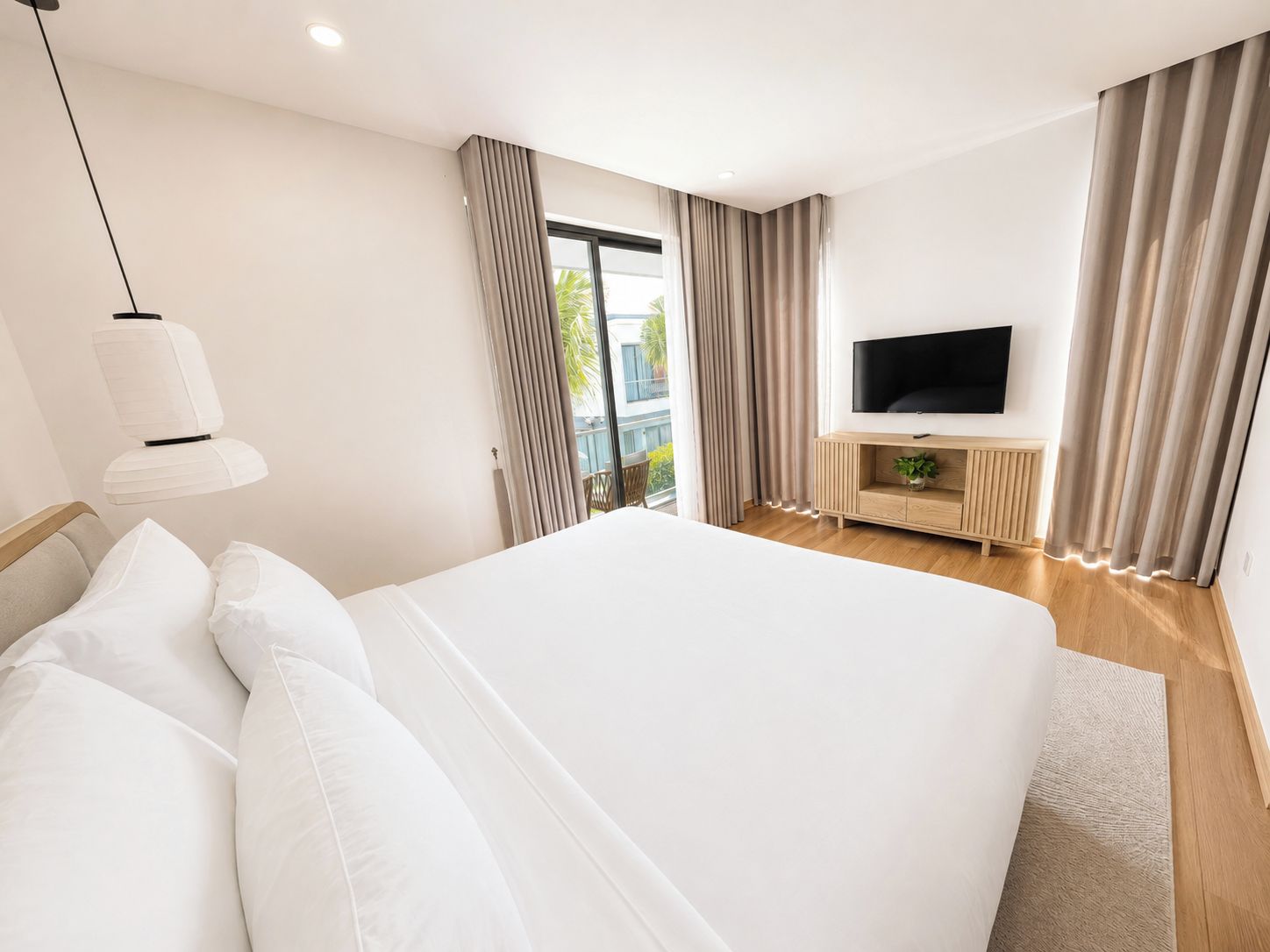 Habitación de hotel con una cama grande, un televisor sobre una consola de madera y vistas al exterior.