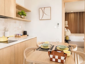 A modern kitchen with wooden cabinets, a countertop, and a dining area with a table set for two. - Sonasea Villas Collection Lagom  (Phu Quoc)