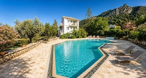 A rectangular swimming pool with a stone border, surrounded by a patio area with lounge chairs and potted plants. - Villa Irini Ocean View 2-bedroom apartment with AC in charming Fryni (Fryni)