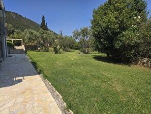 A well-maintained garden with a stone pathway leading to a building, surrounded by lush greenery and trees. - Villa Irini Ocean View 2-bedroom apartment with AC in charming Fryni (Fryni)