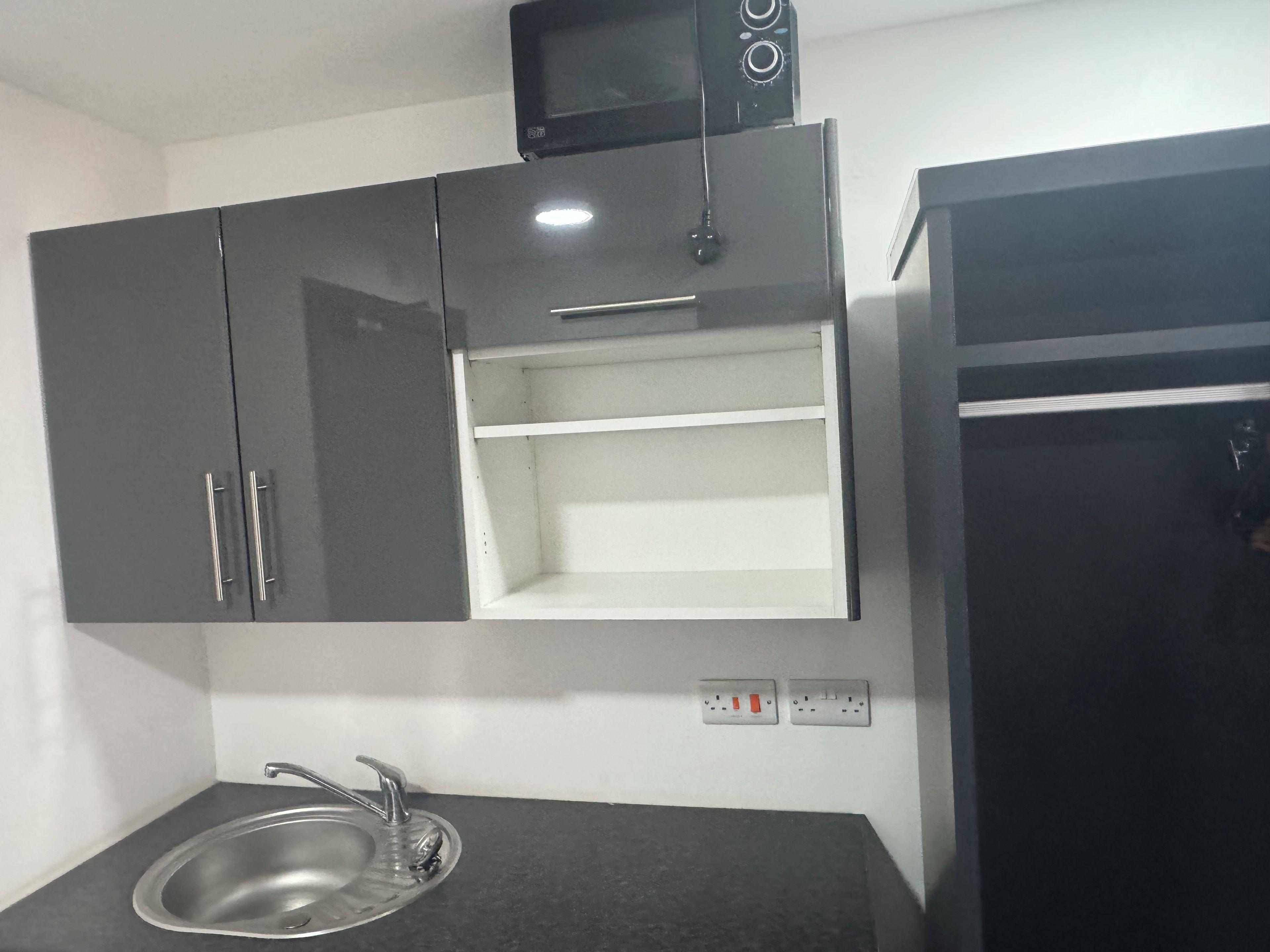 Een keuken met een inbouwmagnetron, een spoelbak met kraan en een koelkast.