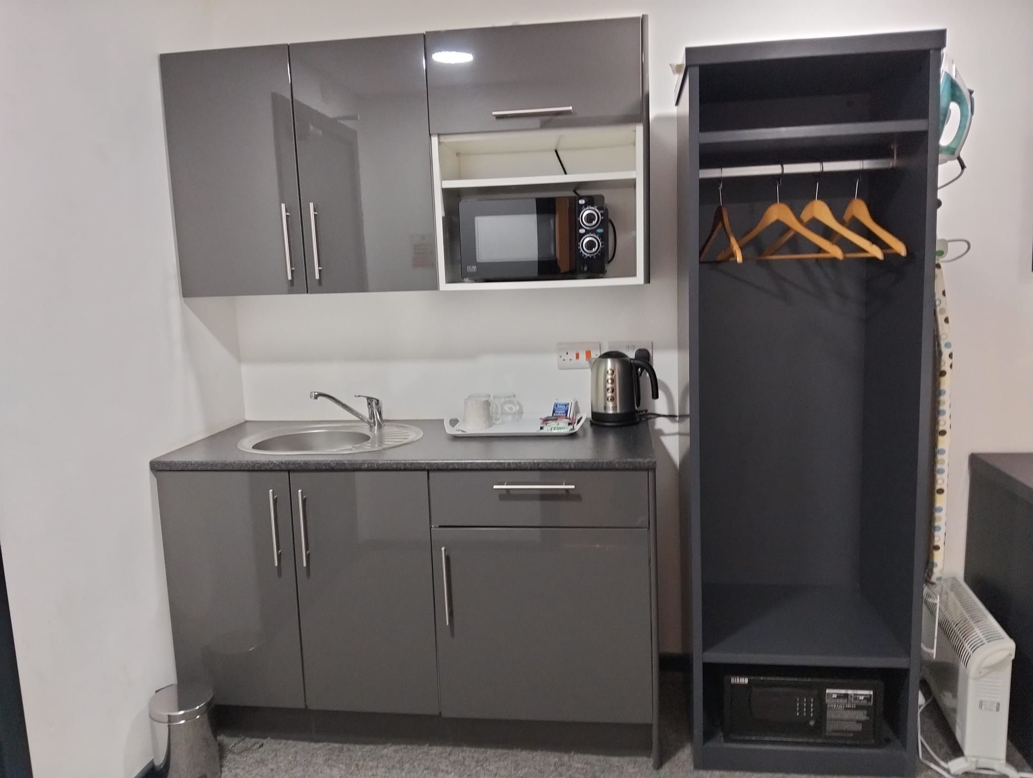 Een kleine keuken met een magnetron, spoelbak en een klein plankje.